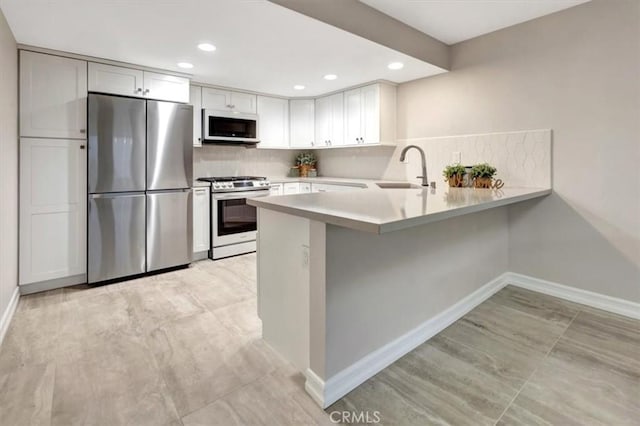kitchen with stainless steel appliances, light countertops, a sink, decorative backsplash, and a peninsula