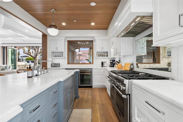 kitchen with white cabinets, high end stainless steel range oven, beverage cooler, and custom range hood