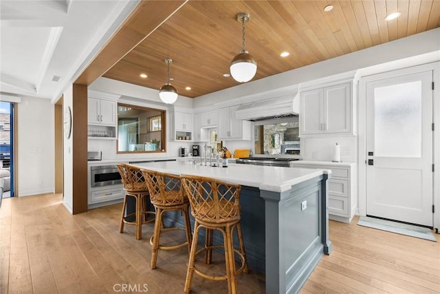 kitchen with white cabinets, a kitchen island with sink, light wood-style floors, light countertops, and a breakfast bar area