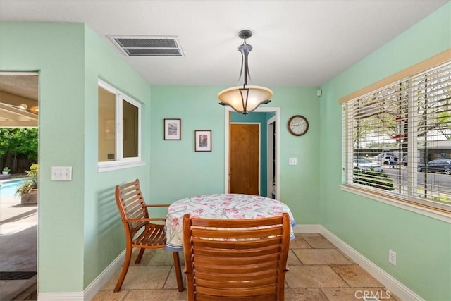 dining space featuring stone tile flooring, visible vents, and baseboards