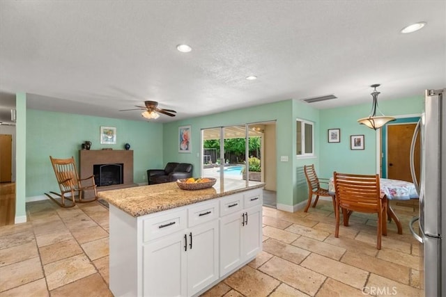 kitchen featuring white cabinets, freestanding refrigerator, stone tile floors, and visible vents