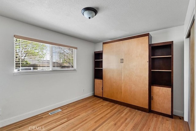 unfurnished bedroom with a textured ceiling, a closet, light wood-style floors, baseboards, and visible vents