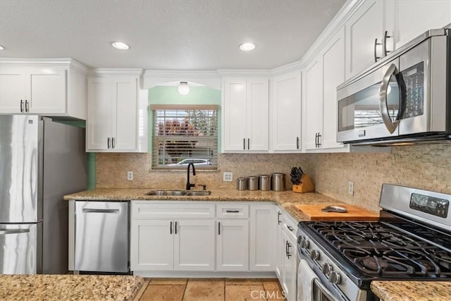kitchen featuring light stone counters, a sink, white cabinets, backsplash, and appliances with stainless steel finishes