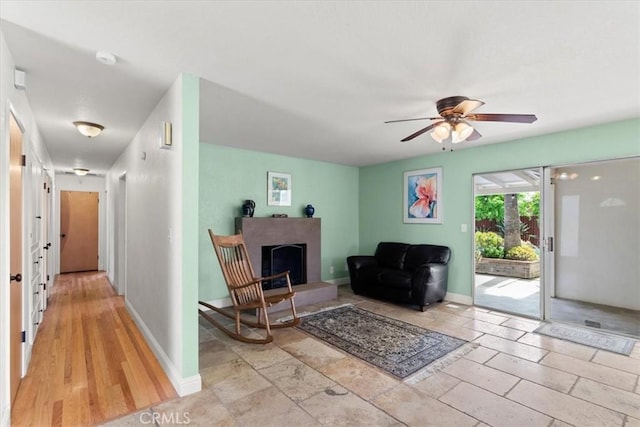 living area with baseboards, a ceiling fan, and a fireplace with raised hearth