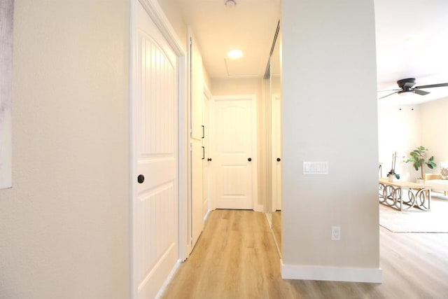 hall featuring attic access, light wood finished floors, and baseboards
