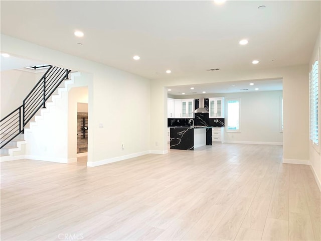 unfurnished living room featuring baseboards, stairs, light wood-type flooring, and recessed lighting