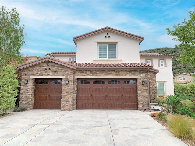 mediterranean / spanish-style house with a tile roof, driveway, stone siding, an attached garage, and stucco siding