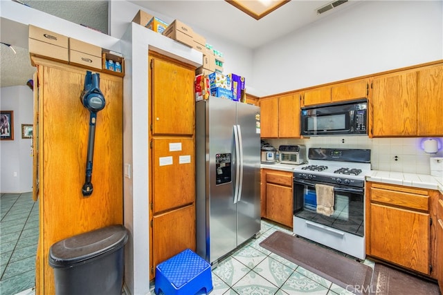 916 Award Dr, Colton, CA 92324 - kitchen featuring stainless steel refrigerator with ice dispenser, black microwave, gas stove, light tile patterned flooring, and brown cabinets