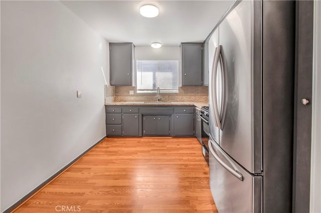 kitchen featuring black range with gas stovetop, freestanding refrigerator, a sink, and gray cabinets