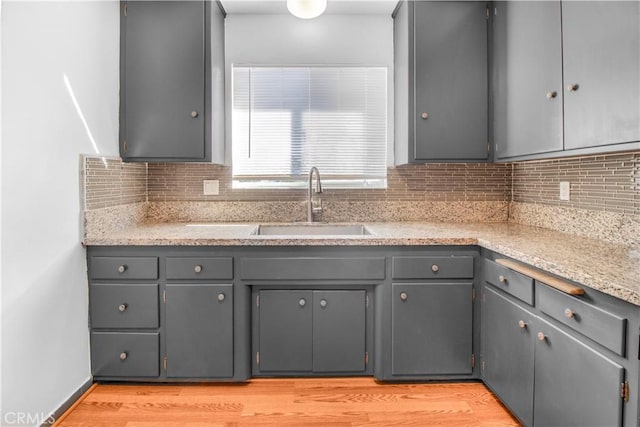 kitchen featuring tasteful backsplash, light wood finished floors, gray cabinets, and a sink