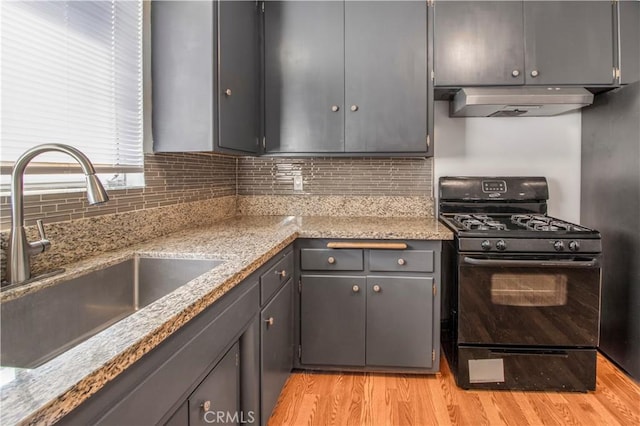 kitchen with light wood finished floors, under cabinet range hood, a sink, black gas stove, and tasteful backsplash