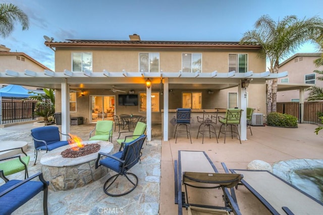 rear view of house featuring fence, a pergola, stucco siding, outdoor dry bar, and an outdoor fire pit