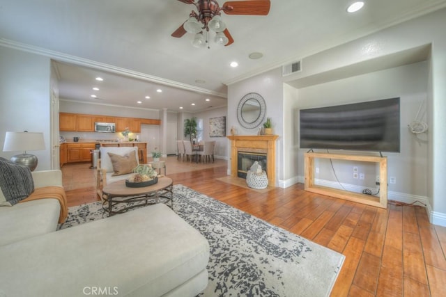 living area with ceiling fan, visible vents, ornamental molding, and light wood-style flooring