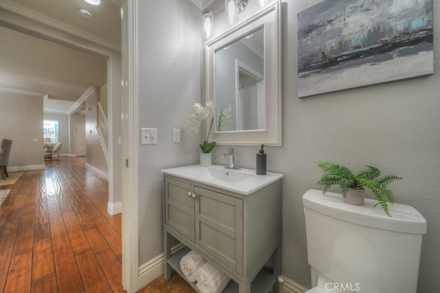 bathroom featuring vanity, toilet, hardwood / wood-style floors, baseboards, and ornamental molding