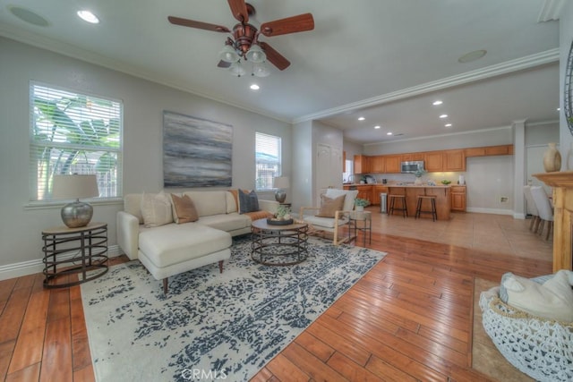 living area featuring light wood-style floors, ornamental molding, and a ceiling fan