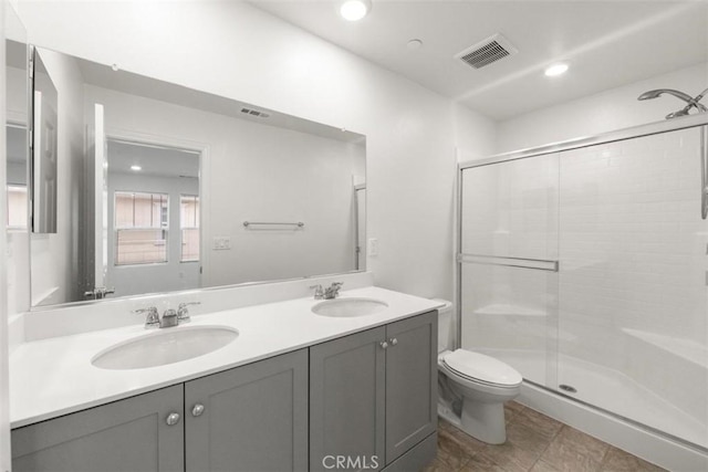 bathroom featuring toilet, visible vents, a sink, and a stall shower