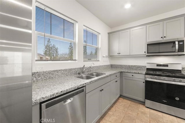 kitchen with appliances with stainless steel finishes, gray cabinets, light stone counters, and a sink