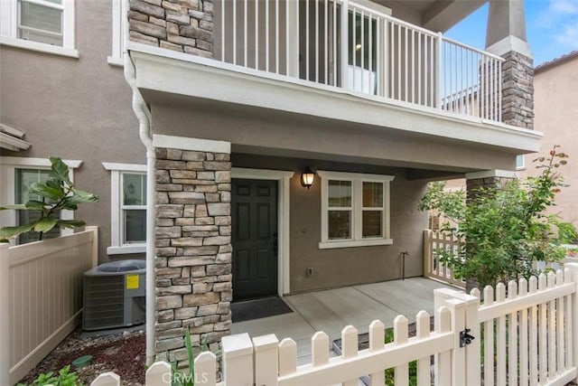 view of exterior entry with central air condition unit, a porch, stone siding, and stucco siding