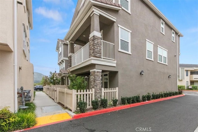 view of side of home with fence, a balcony, and stucco siding