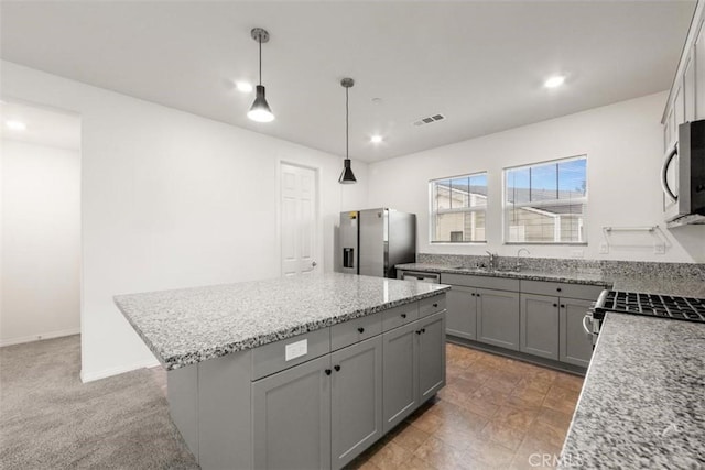 kitchen with stainless steel appliances, visible vents, gray cabinets, light stone countertops, and a kitchen island