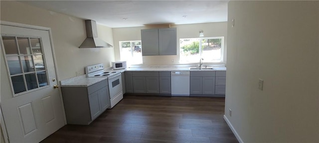 kitchen featuring dark wood-style floors, light countertops, wall chimney range hood, a sink, and white appliances