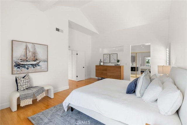 bedroom with baseboards, visible vents, wood finished floors, and high vaulted ceiling