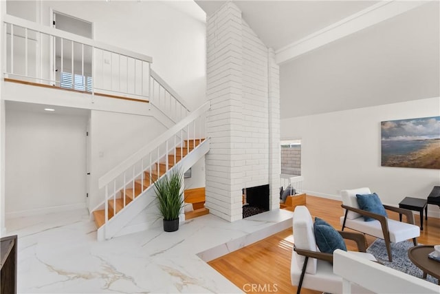 living room featuring stairway, a fireplace, high vaulted ceiling, marble finish floor, and baseboards