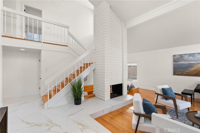 living area featuring stairway, marble finish floor, a brick fireplace, baseboards, and high vaulted ceiling