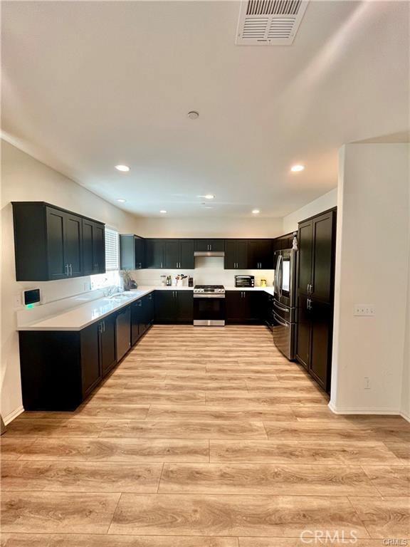 2819 La Calle Sabio Ave, Rosamond, CA 93560 - kitchen with stainless steel gas stove, fridge, light wood-type flooring, light countertops, and recessed lighting