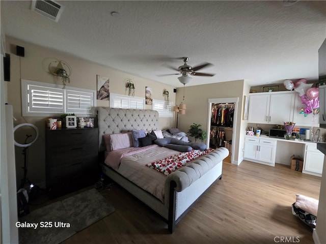 24236 Cahuilla Rd, Apple Valley, CA 92307 - bedroom with a walk in closet, light wood-type flooring, a textured ceiling, a closet, and a ceiling fan