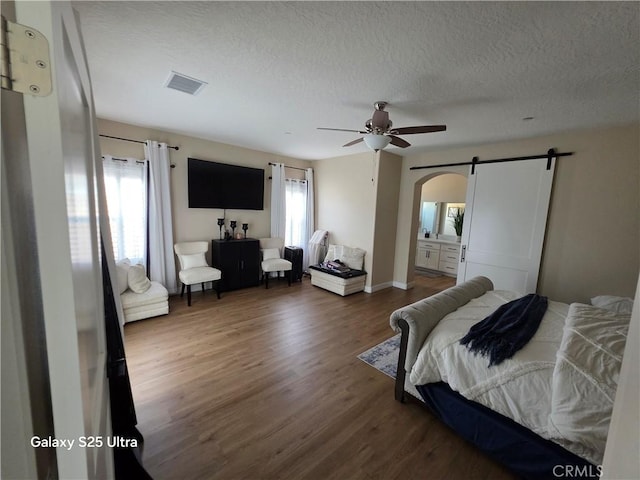 24236 Cahuilla Rd, Apple Valley, CA 92307 - bedroom featuring wood finished floors, arched walkways, a barn door, a textured ceiling, and ceiling fan