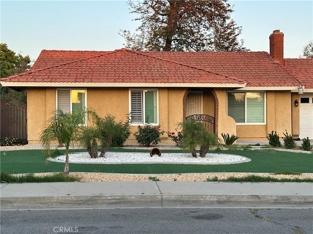 view of front facade featuring a tiled roof, a chimney, a front lawn, and stucco siding