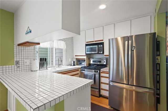 11 Northwind Ct Unit 41, Newport Beach, CA 92663 - kitchen with appliances with stainless steel finishes, a peninsula, tile countertops, white cabinets, and decorative backsplash