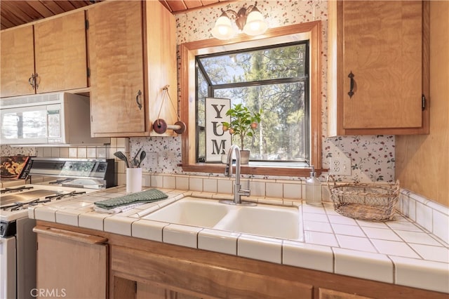 kitchen featuring gas range, a sink, white microwave, and tile countertops