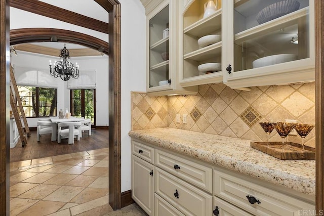 5015 Rancho Quinta Bnd, San Diego, CA 92130 - kitchen featuring a chandelier, light stone counters, glass insert cabinets, tasteful backsplash, and white cabinets
