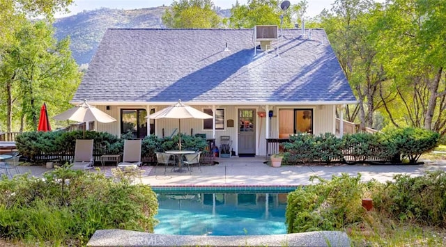 rear view of property featuring roof with shingles, a patio area, and a fenced in pool