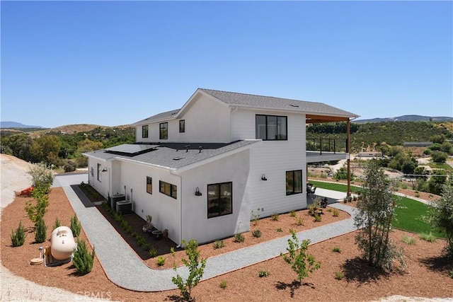 exterior space with central AC, a balcony, a mountain view, stucco siding, and solar panels
