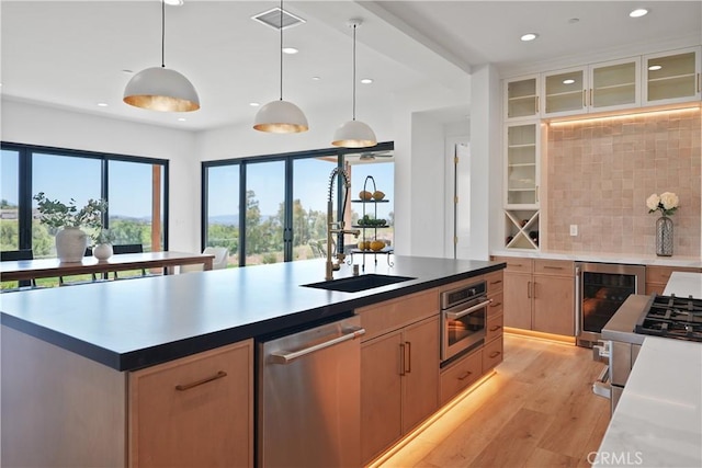 kitchen featuring stainless steel appliances, light wood-style flooring, a sink, backsplash, and beverage cooler
