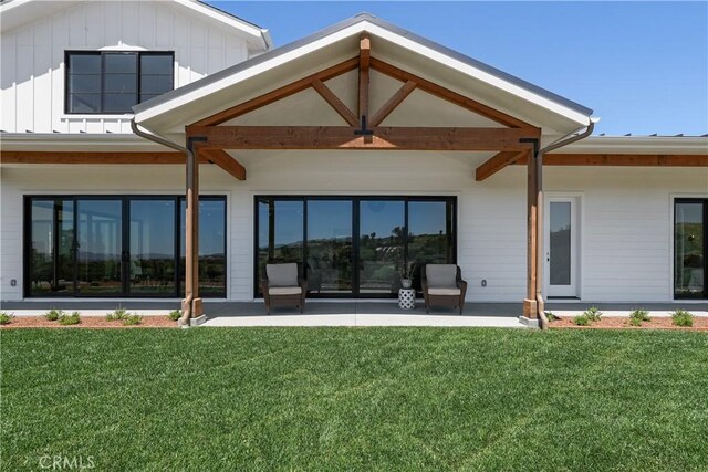 rear view of property featuring board and batten siding, a patio area, and a lawn
