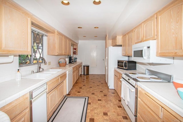 kitchen featuring tile counters, light brown cabinetry, a sink, and white appliances