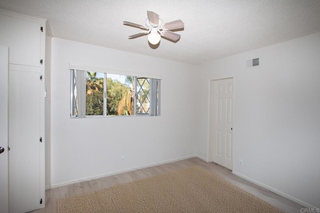 unfurnished room with light wood-style flooring, a textured ceiling, baseboards, visible vents, and a ceiling fan