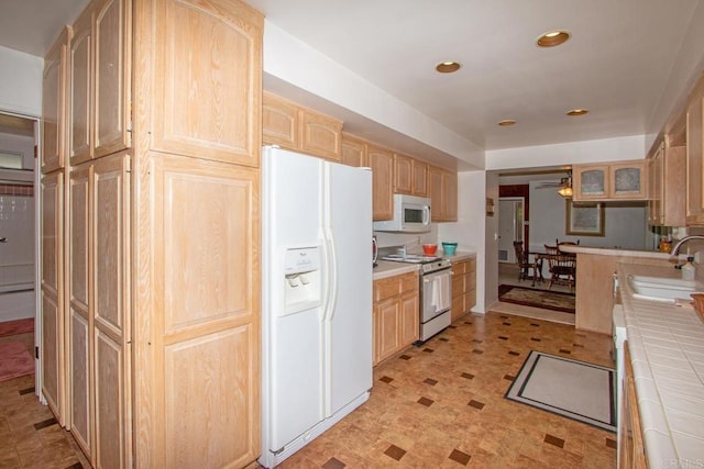 kitchen with light brown cabinets, tile counters, a sink, white appliances, and ceiling fan