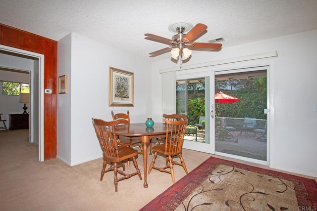 dining space featuring visible vents, light colored carpet, a textured ceiling, and ceiling fan