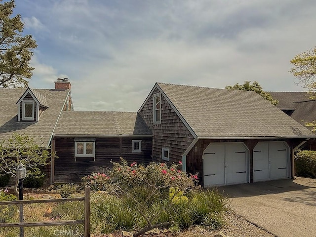exterior space with a chimney, an attached garage, driveway, and roof with shingles