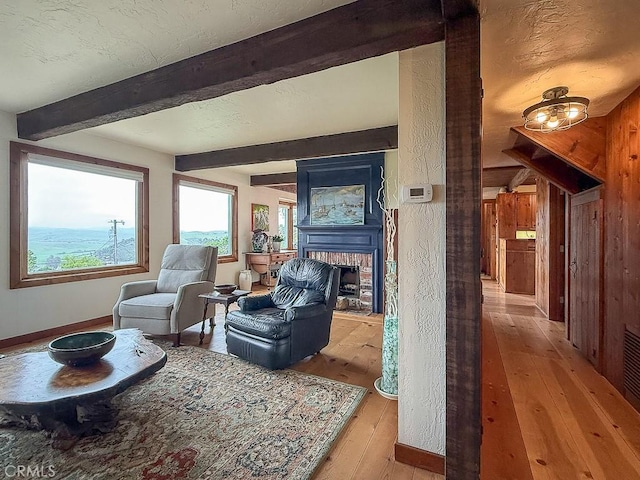 living area with baseboards, a brick fireplace, light wood-style floors, and beamed ceiling