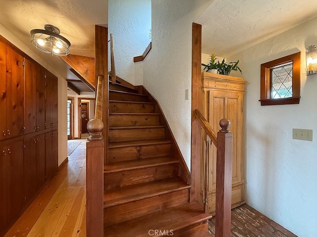 staircase with wood-type flooring, a textured wall, and a textured ceiling