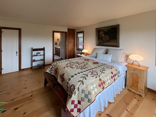 bedroom featuring baseboards, ensuite bathroom, and light wood finished floors