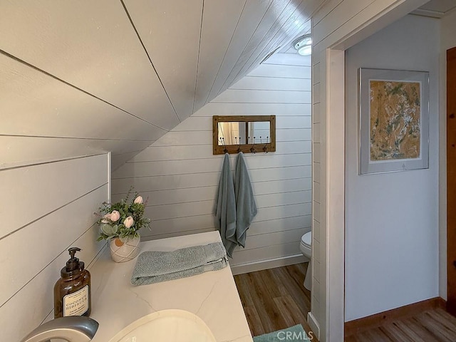 bathroom featuring wooden walls, lofted ceiling, toilet, and wood finished floors
