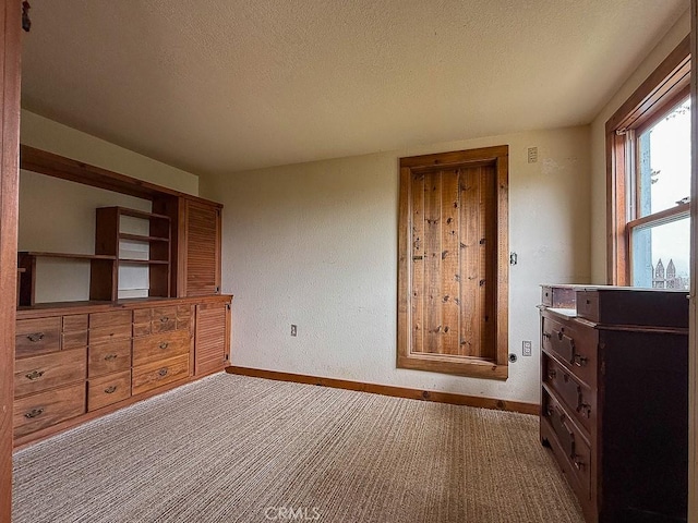 unfurnished bedroom with a textured ceiling, carpet flooring, and baseboards