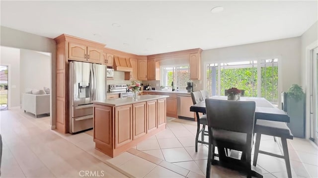 kitchen with light brown cabinets, stainless steel appliances, a sink, light countertops, and an island with sink
